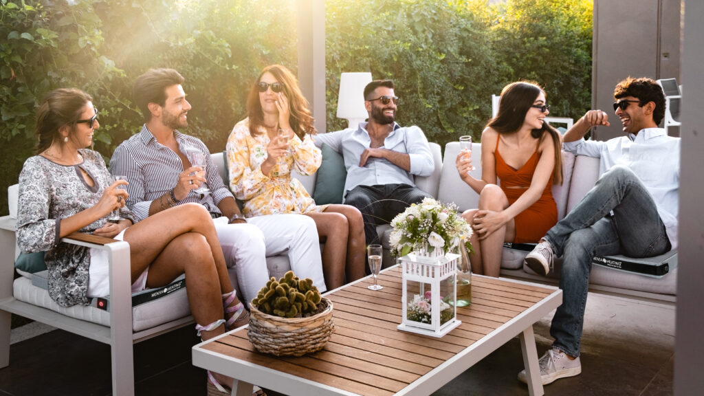 Group of cheerful young people carefree sitting together drinkin